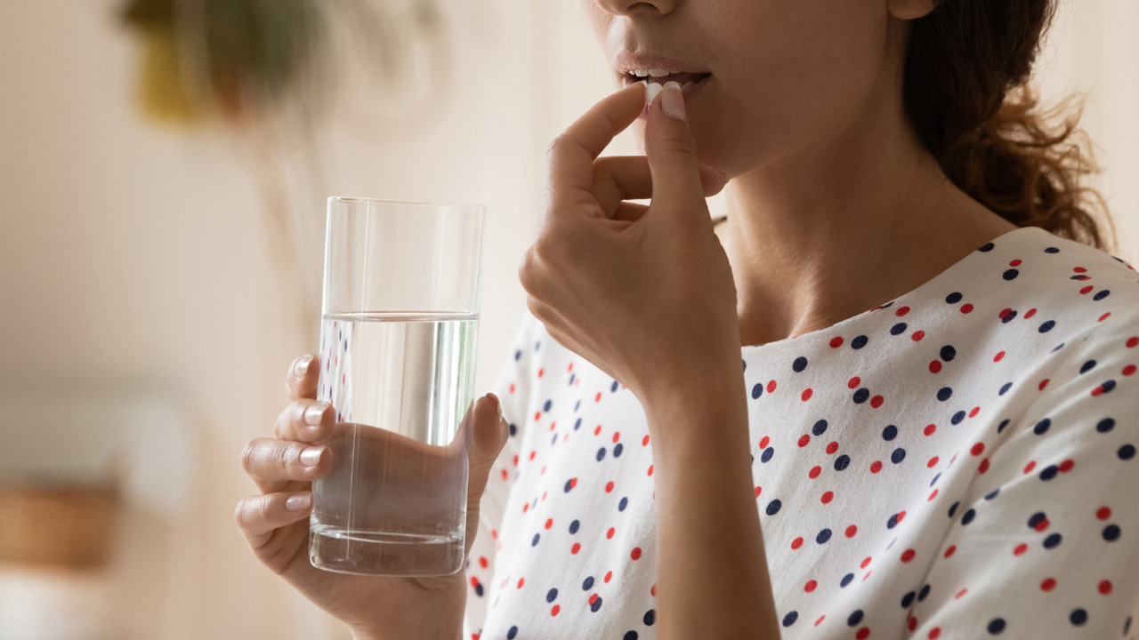 Donna che assume una compressa con un bicchiere d’acqua, simbolo dell’uso di antidolorifici oppiacei ed oppioidi e dell’importanza di un’assunzione responsabile.